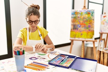 Sticker - Young brunette teenager at art studio checking the time on wrist watch, relaxed and confident