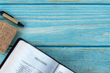 Proverbs open Holy Bible Book on a blue wooden background with a notebook and pen. Top table view. Copy space. Study Scriptures for wisdom by God Jesus Christ. Christian biblical concept.