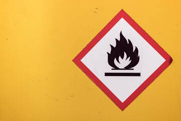 Traditional white, red and black flammable fire icon diamond sticker against a bright yellow wall.