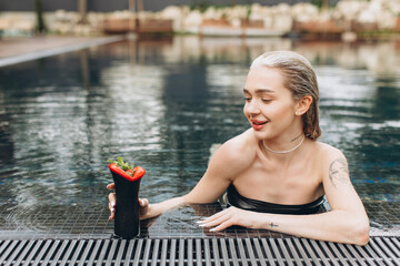 Wall Mural - The beautiful and stylish blond woman relaxing in the pool with a cocktail in summer