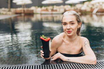 Wall Mural - The beautiful and stylish blond woman relaxing in the pool with a cocktail in summer