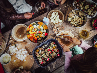 top view of group of friends preparing, cutting and eating vegetables and salads together for vegan grill bbq party on a rustig table outside