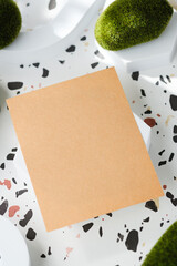 Poster - kraft paper on white geometric pedestal on terrazzo background with summer sunlight and moss rock