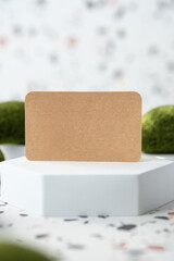 Poster - kraft paper on white geometric pedestal on terrazzo background with summer sunlight and moss rock