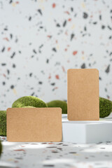 Poster - kraft paper on white geometric pedestal on terrazzo background with summer sunlight and moss rock