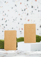 Poster - kraft paper on white geometric pedestal on terrazzo background with summer sunlight and moss rock