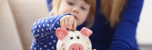 A Little Girl Puts A Coin In A Pink Piggy Bank