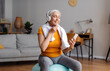 © Prostock-studio - Happy senior woman with wireless headset sitting on fitball, listening to music on phone, resting during home workout