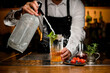 Close-up view of glass with cocktail and sprig of mint in which bartender adds liquid from siphon