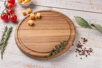 Wall Mural - round wooden cutting board with edging. cherry tomatoes, slices of cheese and spices on a white background. mockup with copy space for text, side view