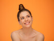 Happy dreaming woman looking up, isolated portrait on orange back with happy girl bare shoulders and bunch hair dress. Female emotional face.