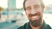 Closeup Portrait Of Smiling Man With A Beard On An Urban City Background. Frontal Close-up Of Happy Young Hipster Male Looking At Camera