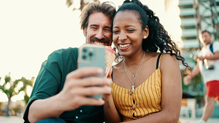 portrait of happy man and smiling woman watching video on smartphone. Close-up of joyful young interracial couple browsing photos on mobile phone on urban city background