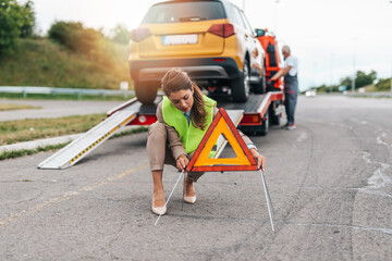 Wall Mural - Middle age business woman after car accident putting safety or warning foldable triangle on the road. Help on the road concept.