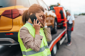 Wall Mural - Elegant middle age business woman calling someone while towing service helping her on the road. Roadside assistance concept.