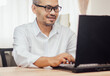 © vachiravit - Happy man wearing glasses and smiling as he works on his black laptop where business is going well.