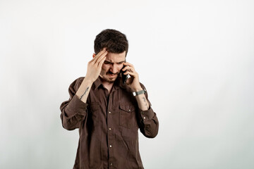 Wall Mural - Happy young man wearing shirt posing isolated over white background feeling upset desperate talking on the phone having problems. Hearing bad news during mobile conversation.