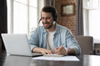 © fizkes - Smiling millennial man wear headset take part in educational webinar, on-line lesson, remote effective english course makes notes sit at desk with laptop. Virtual meeting, tuition, e-learning concept