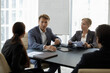 © fizkes - Middle-aged boss in suit lead corporate meeting with staff members sit at desk in modern office boardroom, search business solutions, take part in negotiations or group seminar event. Coaching concept
