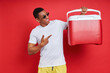 Happy mixed race man pointing cooler box while standing against red background