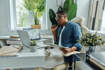 Thoughtful young mixed race man using technologies while working in the office