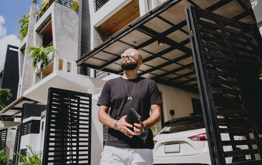 Young businessman walking out of his modern home with garage and car