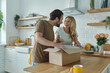 © gstockstudio - Beautiful young couple unpacking box and smiling while standing at the domestic kitchen
