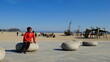 Fröhliche hübsche Asiatin sitzt auf Stein am Sandstrand bei Travemünde mit schönem Abenteuerspielplatz