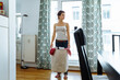 young brunette woman spends time at home doing household chores, standing in middle of apartment, holding fabric laundry basket filled with clothes