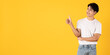 Smiling young asian teenage man wearing white shirt and jeans on yellow background giving thumbs up