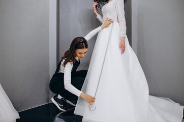 Wall Mural - Female making adjustment to wedding gown in fashion designer studio. Bride wearing her wedding gown with female dress designer making final adjustments on dress.