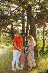 Wall Mural - Happy family on summer walk, Mother, father and daughters walking in the Park and enjoying the beautiful nature.