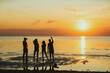 Silhouettes of four friends cheering with beer bottles standing in sea water on beach during beautiful orange sunset and celebrating life, rear view backlit shot