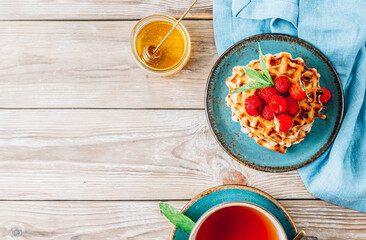 Stack of belgian waffles with honey, mint and fresh raspberries on turqouise plate