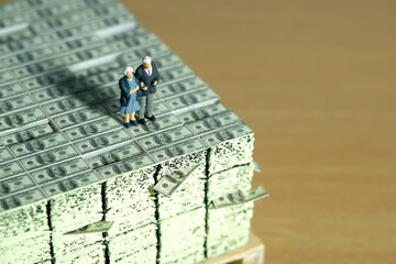 Miniature people toys conceptual photography. Elderly couple standing above pile of money cash. Finance and saving concept