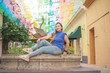 © sandor - Street portrait of young woman looking at camera with multicolored flags in background.