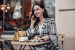 Attractive young female talking on cellphone while having coffee with cheesecake at cafe.