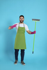 Wall Mural - Young man with green broom on light blue background