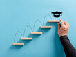 Male hand arranges a wooden block ladder with academic cap symbol. Graduation achievement and education goals.
