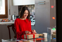 Happy Young Woman Tying Ribbon On Gift Box At Home