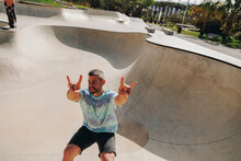 Man Showing Horn Sign And Skateboarding On Sports Ramp