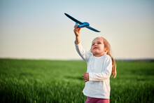 Playful Girl Flying Airplane Toy On Field At Sunset