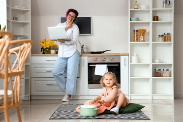 Poster - little girl with spoon, toy, cooking pot and her working mother in kitchen