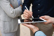 © Westend61 - Hand of businessman signing on tablet PC standing by colleagues