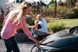 © Westend61 - Woman charging electric car with man sitting with daughter on wall