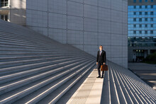 Businessman Holding Bag Standing On Staircase In Front Of Building