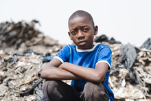 Pensive Young African Waste Collector Boy Sitting Tired On Top Of A Pile Of Plastic Trash In A Landfill Contemplating The Ugly Surroundings; Concept Of Poverty, Child Exploitation And Human Inequality