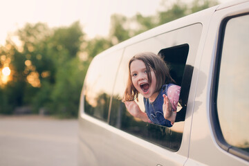 Funny European kid girl peeking out of window of minivan, family trips with children