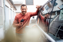 Smiling Man Holding Charging Cable Leaning On Electric Car