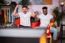 Cheerful Young Friends Watching Football Match Gesturing Fists Sitting On Sofa At Home